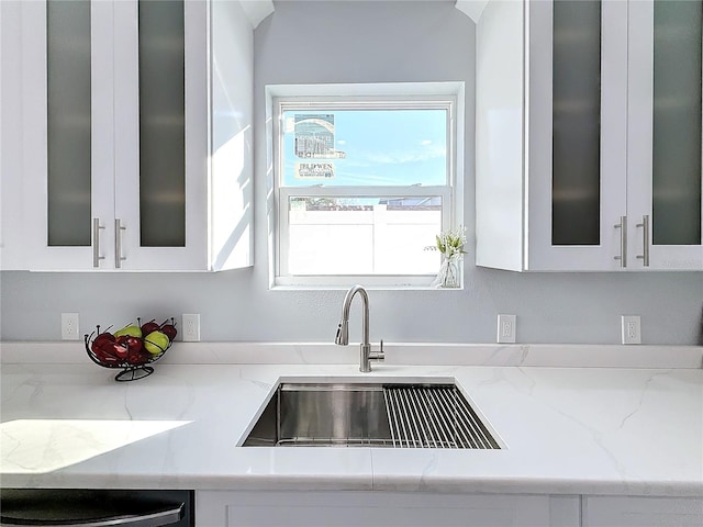 kitchen with light stone countertops, sink, and white cabinets