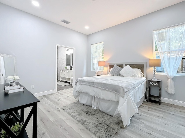 bedroom featuring connected bathroom, multiple windows, and light hardwood / wood-style flooring