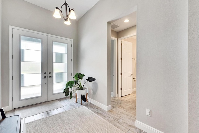 entryway with french doors, light hardwood / wood-style floors, and a notable chandelier