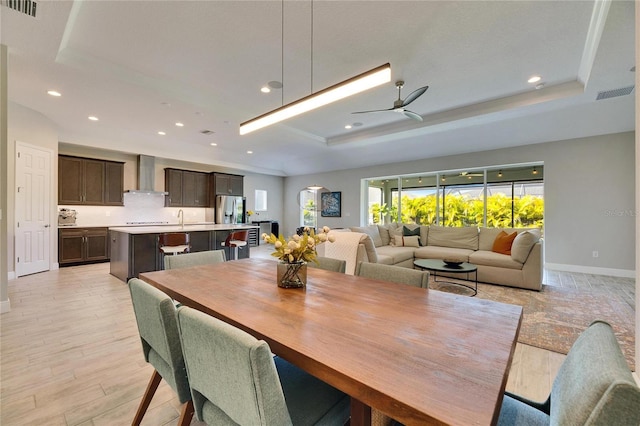 dining area featuring sink, a tray ceiling, ceiling fan, and light wood-type flooring