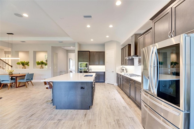 kitchen with an island with sink, hanging light fixtures, dark brown cabinetry, stainless steel appliances, and light wood-type flooring