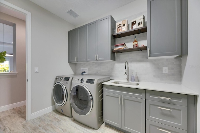 laundry area featuring cabinets, washer and clothes dryer, sink, and light wood-type flooring