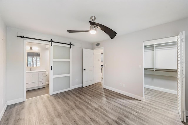 unfurnished bedroom featuring a barn door, visible vents, light wood-style flooring, and baseboards