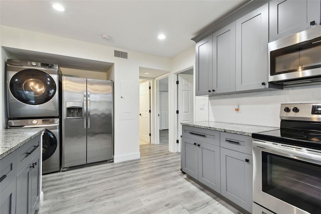 kitchen with light wood finished floors, visible vents, appliances with stainless steel finishes, stacked washer / drying machine, and light stone countertops