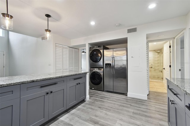 kitchen featuring gray cabinets, stacked washer and clothes dryer, stainless steel fridge, and decorative light fixtures