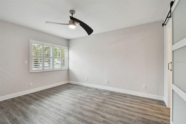 unfurnished room featuring a barn door, baseboards, a ceiling fan, and wood finished floors