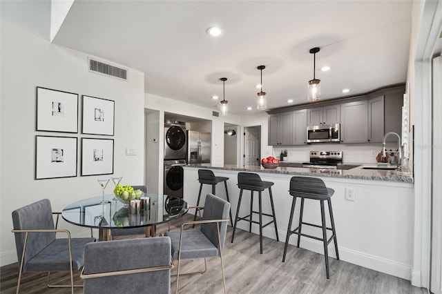 kitchen featuring a peninsula, stacked washer / dryer, a sink, visible vents, and appliances with stainless steel finishes