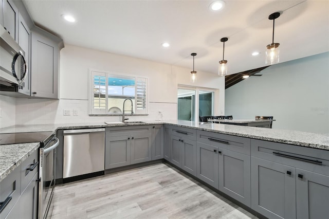 kitchen with a sink, appliances with stainless steel finishes, gray cabinets, light stone countertops, and decorative light fixtures