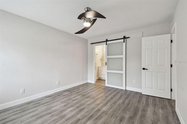 unfurnished bedroom with baseboards, ensuite bath, light wood finished floors, and a barn door