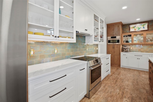 kitchen with appliances with stainless steel finishes, light stone countertops, white cabinets, decorative backsplash, and light wood-type flooring