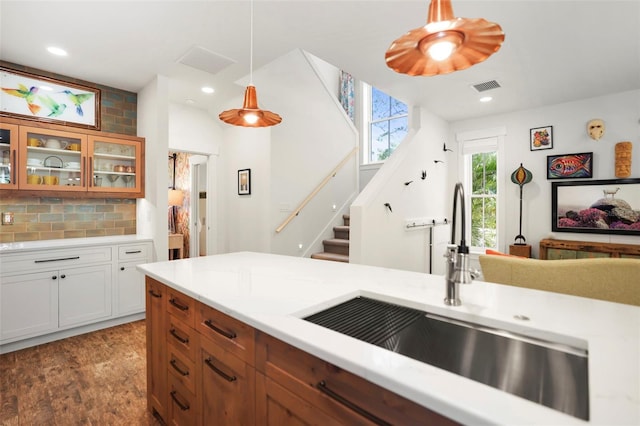 kitchen featuring pendant lighting, light countertops, visible vents, glass insert cabinets, and a sink