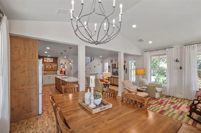 dining space featuring lofted ceiling, sink, an inviting chandelier, and light hardwood / wood-style flooring