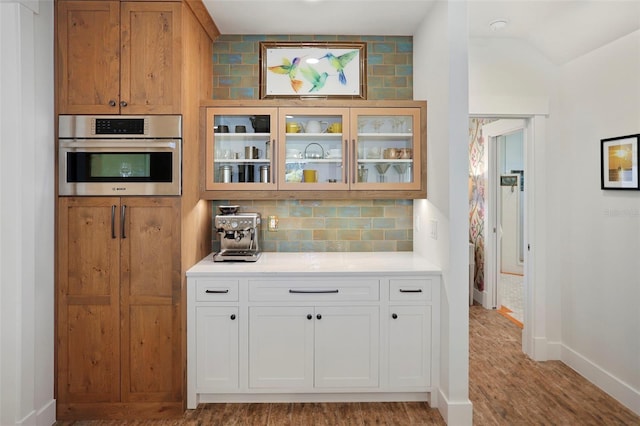 kitchen featuring backsplash, oven, light wood-type flooring, and white cabinets