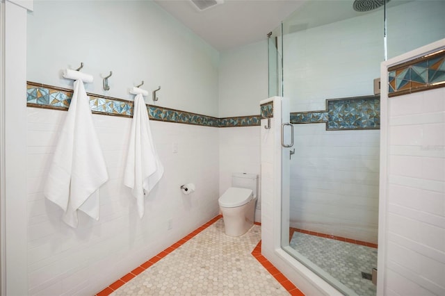 bathroom featuring wainscoting, toilet, tile patterned floors, a shower stall, and tile walls