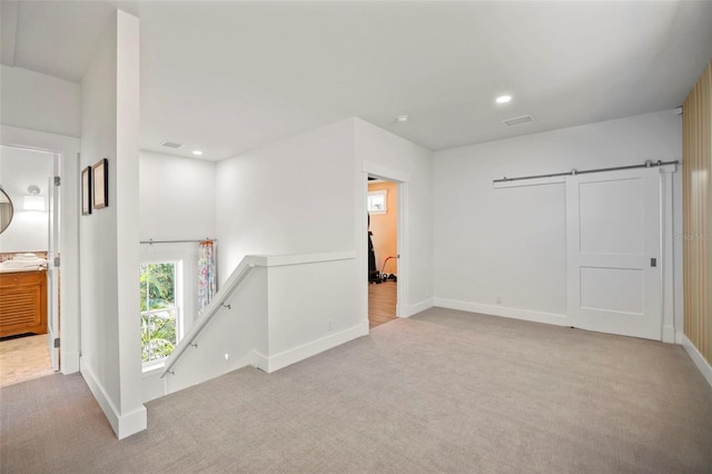 spare room with light carpet, a barn door, visible vents, and recessed lighting