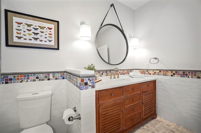 bathroom with toilet, wainscoting, vanity, and tile walls