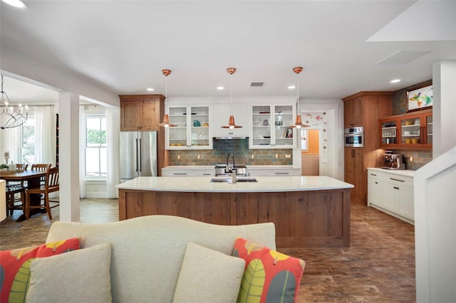 kitchen with pendant lighting, stainless steel appliances, white cabinets, and a center island with sink