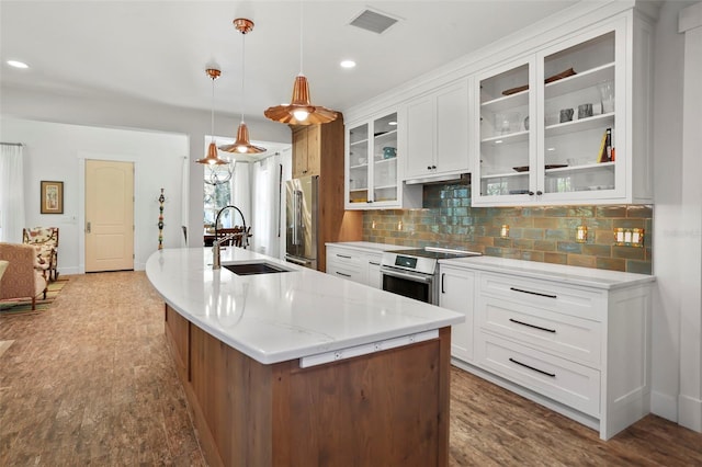 kitchen with glass insert cabinets, decorative light fixtures, a sink, appliances with stainless steel finishes, and a center island with sink