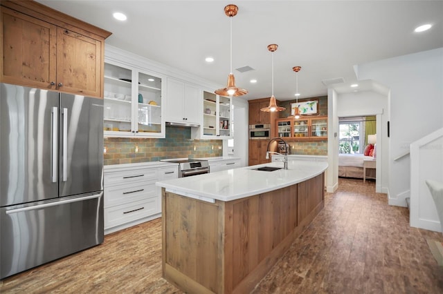 kitchen featuring a center island with sink, stainless steel appliances, light countertops, glass insert cabinets, and white cabinets