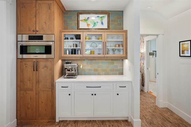 kitchen featuring decorative backsplash, white cabinets, glass insert cabinets, light countertops, and stainless steel oven