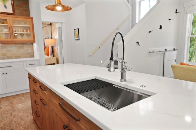 kitchen with pendant lighting, brown cabinets, backsplash, glass insert cabinets, and a sink