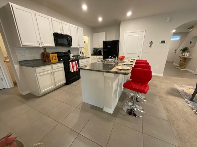 kitchen featuring dark countertops, black appliances, white cabinets, and a sink