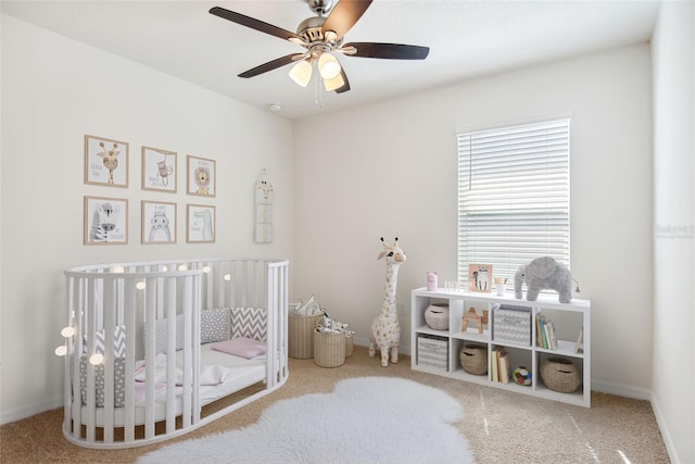 bedroom with ceiling fan, a nursery area, carpet flooring, and baseboards