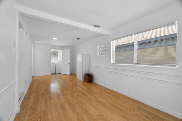 unfurnished room with light hardwood / wood-style flooring, washer and dryer, and beamed ceiling