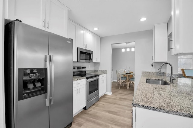 kitchen with sink, white cabinets, stainless steel appliances, light stone countertops, and light wood-type flooring