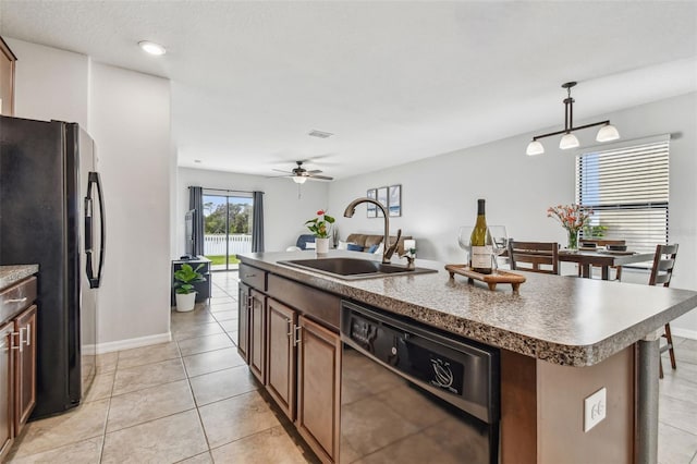 kitchen featuring light tile patterned floors, a kitchen island with sink, a sink, black appliances, and decorative light fixtures