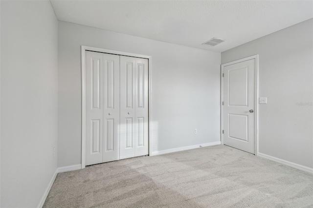 unfurnished bedroom with a closet, light colored carpet, visible vents, and baseboards