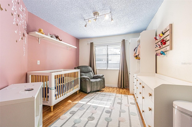 bedroom with a nursery area, rail lighting, light hardwood / wood-style flooring, and a textured ceiling