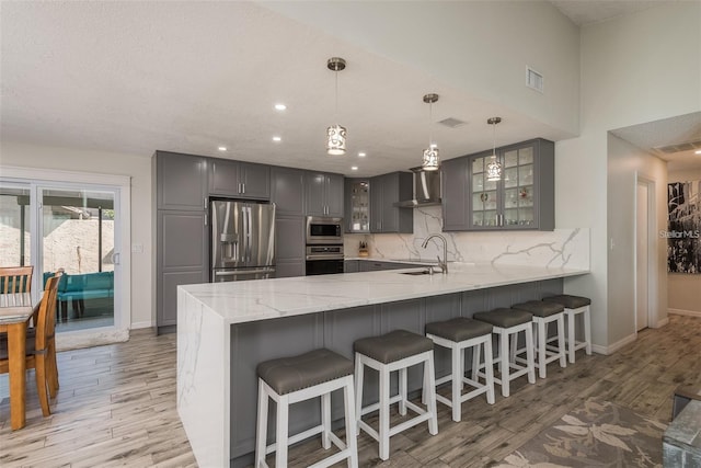 kitchen with tasteful backsplash, hanging light fixtures, light hardwood / wood-style flooring, kitchen peninsula, and stainless steel appliances