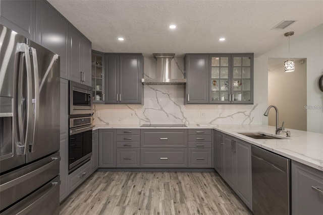 kitchen with sink, gray cabinetry, hanging light fixtures, stainless steel appliances, and wall chimney range hood