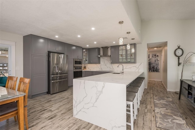 kitchen with wall chimney exhaust hood, decorative light fixtures, gray cabinets, kitchen peninsula, and stainless steel appliances