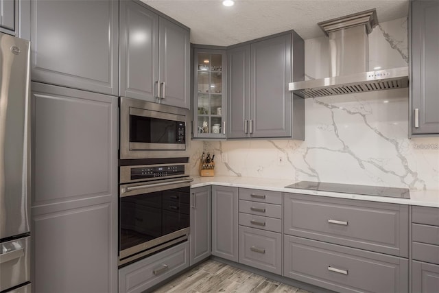 kitchen featuring gray cabinetry, a textured ceiling, light hardwood / wood-style flooring, appliances with stainless steel finishes, and wall chimney range hood