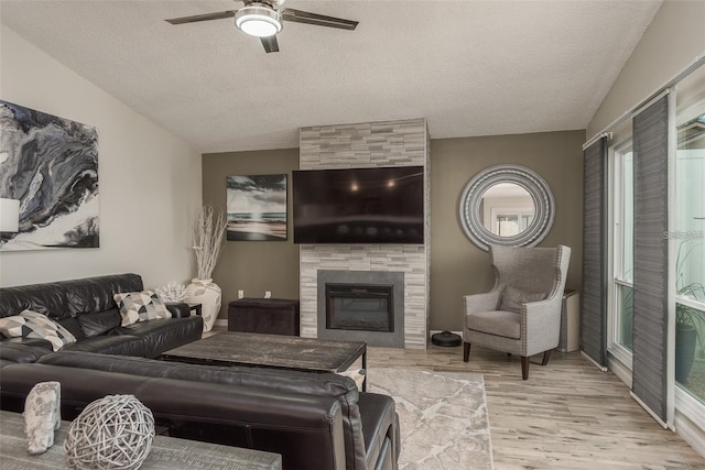 living room featuring lofted ceiling, light hardwood / wood-style flooring, a tile fireplace, and a textured ceiling