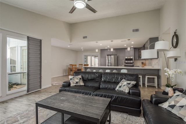 living room with ceiling fan, a towering ceiling, sink, and light hardwood / wood-style floors