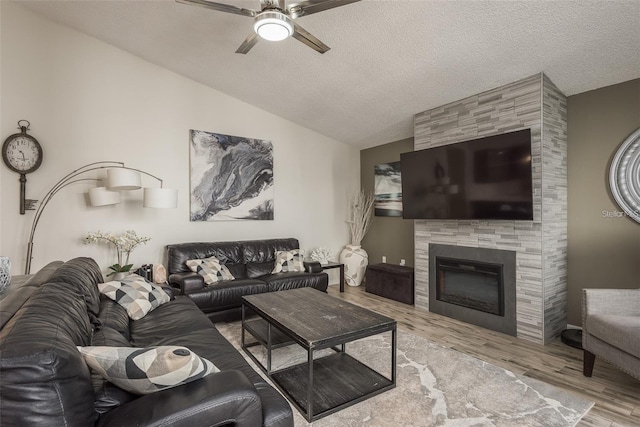 living room with lofted ceiling, a textured ceiling, light wood-type flooring, ceiling fan, and a tiled fireplace