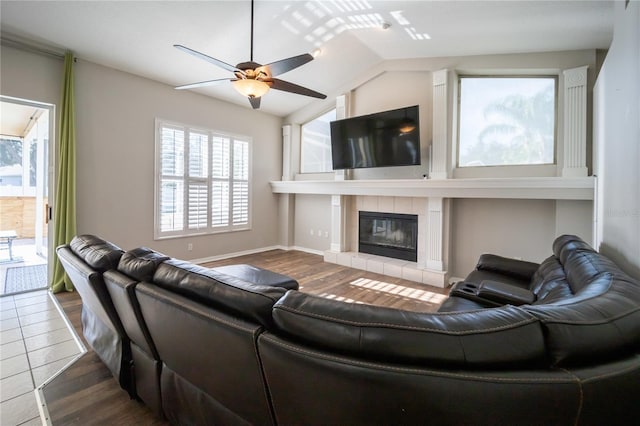 living room with a tiled fireplace, hardwood / wood-style flooring, lofted ceiling, and ceiling fan