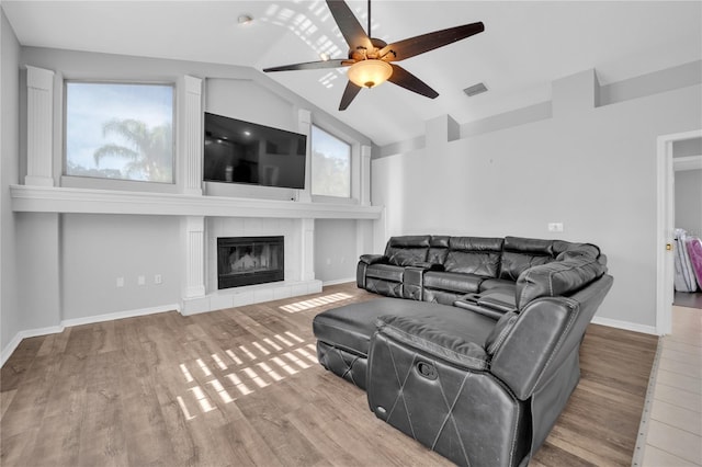 living room featuring ceiling fan, wood-type flooring, vaulted ceiling, and a tile fireplace