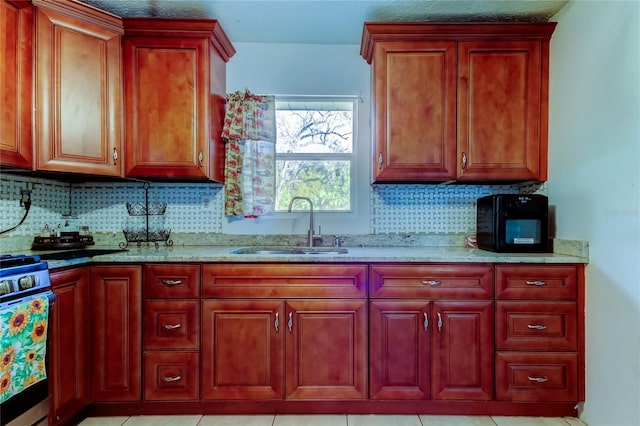 kitchen with sink, stainless steel stove, light tile patterned floors, light stone counters, and tasteful backsplash