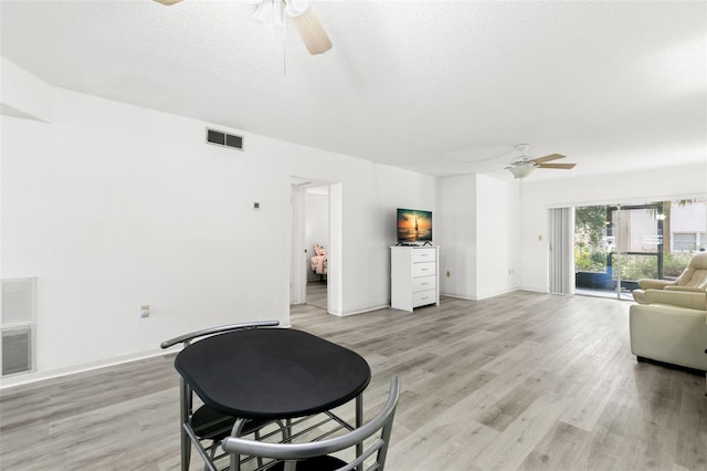 living room with a textured ceiling, ceiling fan, and light wood-type flooring