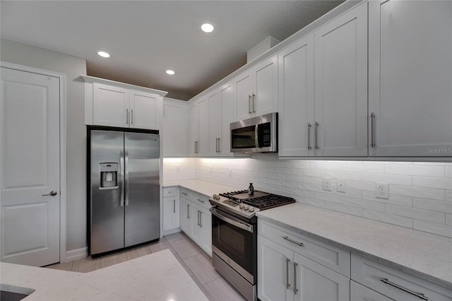 4899 Isola Ct, Wesley Chapel, FL 33543 - kitchen with appliances with stainless steel finishes, white cabinetry, backsplash, light stone counters, and recessed lighting