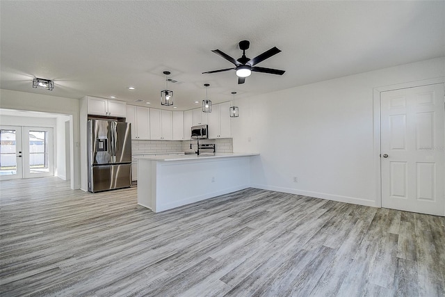 kitchen featuring white cabinetry, decorative light fixtures, appliances with stainless steel finishes, kitchen peninsula, and light hardwood / wood-style floors