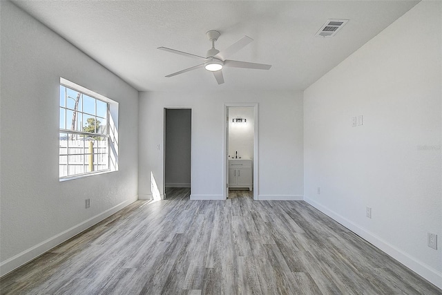 unfurnished bedroom with ceiling fan, connected bathroom, a textured ceiling, and light hardwood / wood-style flooring