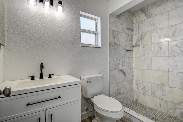 bathroom featuring vanity, a tile shower, and toilet