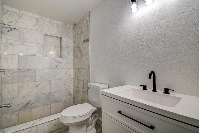 bathroom with vanity, tiled shower, and toilet