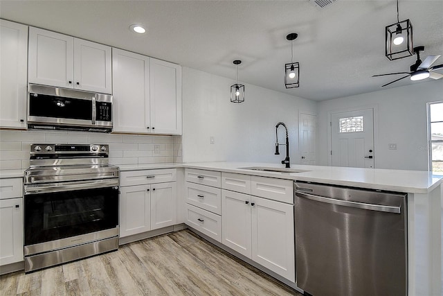 kitchen with sink, hanging light fixtures, kitchen peninsula, stainless steel appliances, and white cabinets