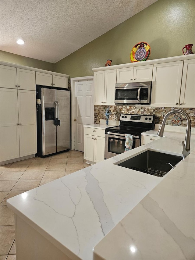 kitchen with light tile patterned floors, light stone countertops, white cabinets, and appliances with stainless steel finishes